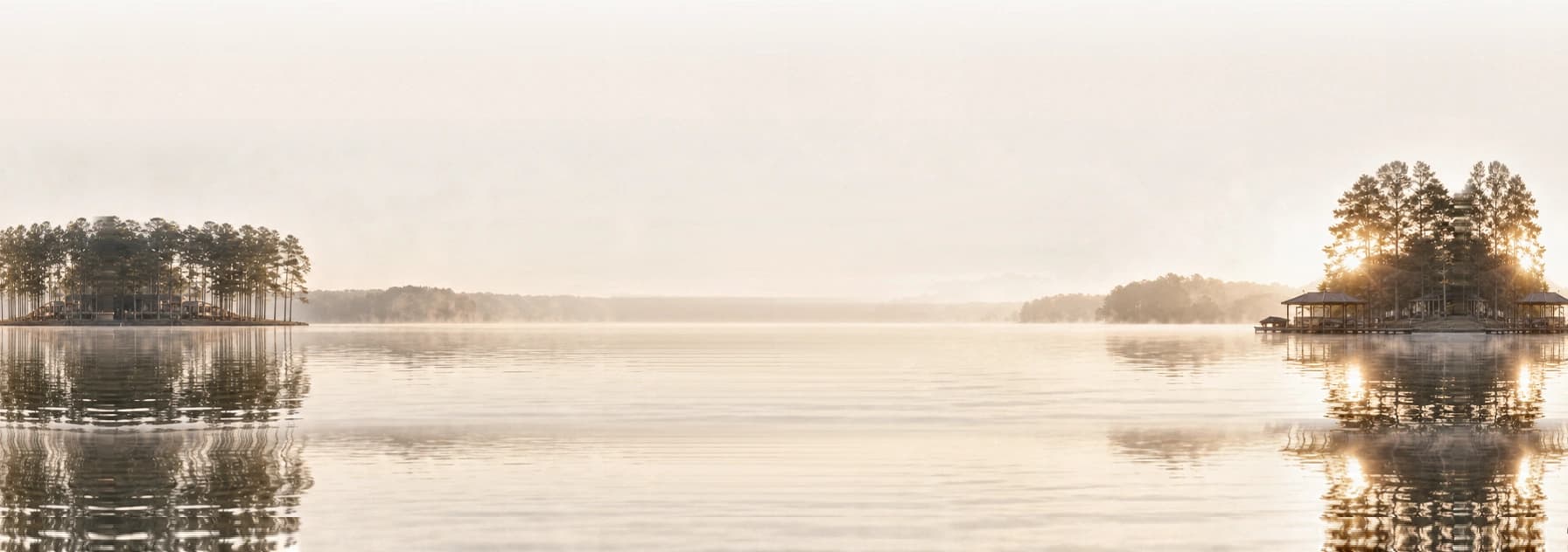 Mist rising off still lake water at dawn, the sun low behind the far shoreline